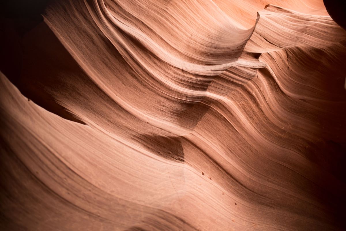 Close view of smooth, curving sandstone walls in warm orange and pink tones, with layered ridges and soft shadows.